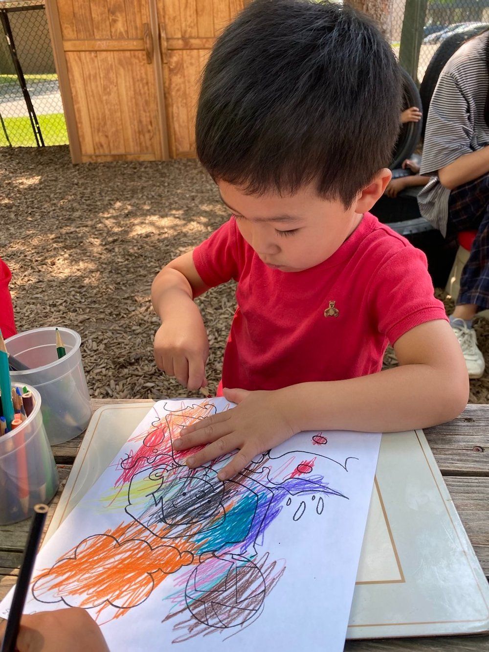 A young boy is sitting at a table drawing with crayons.