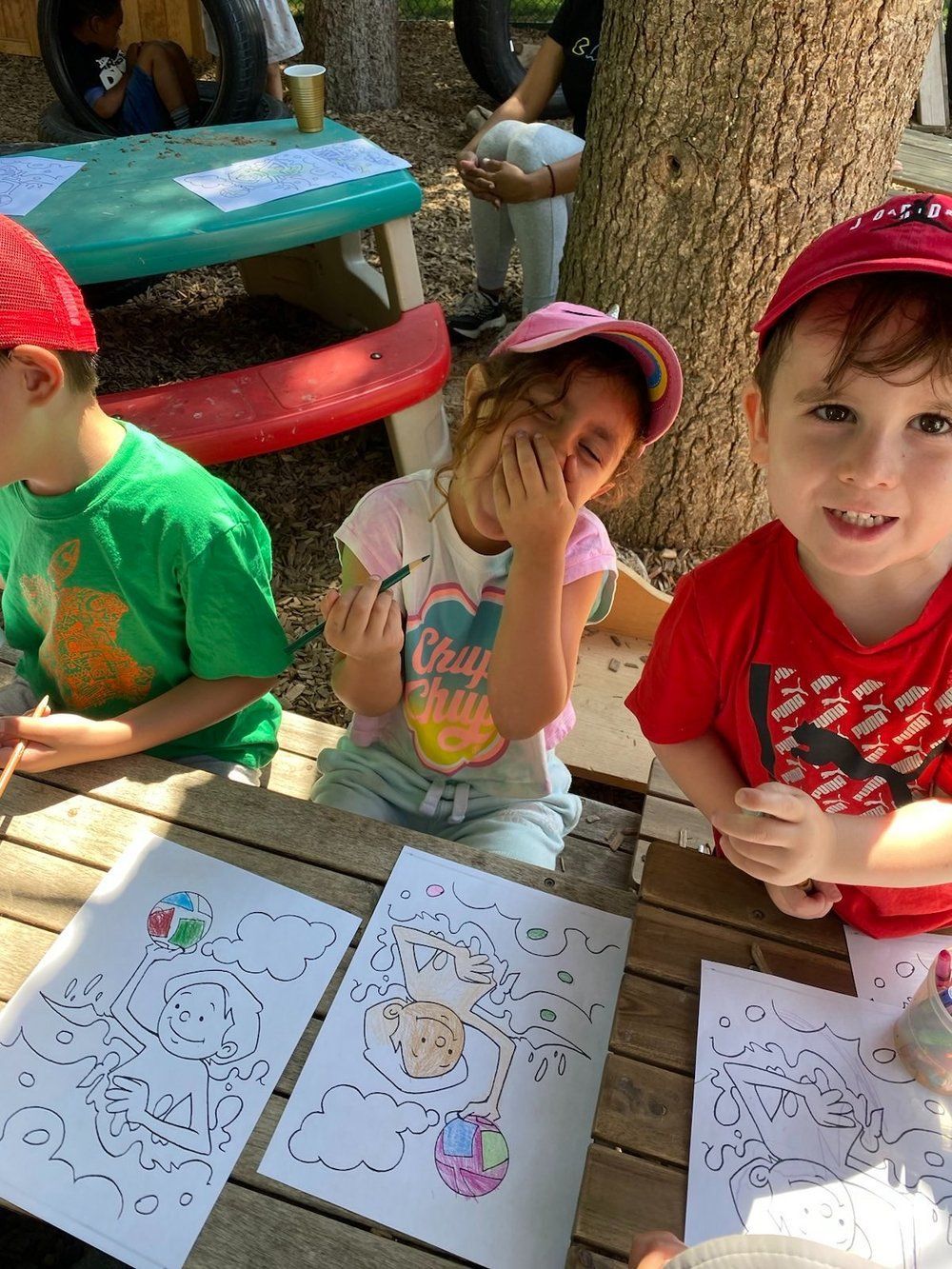 A group of children are sitting at a picnic table with papers on it.