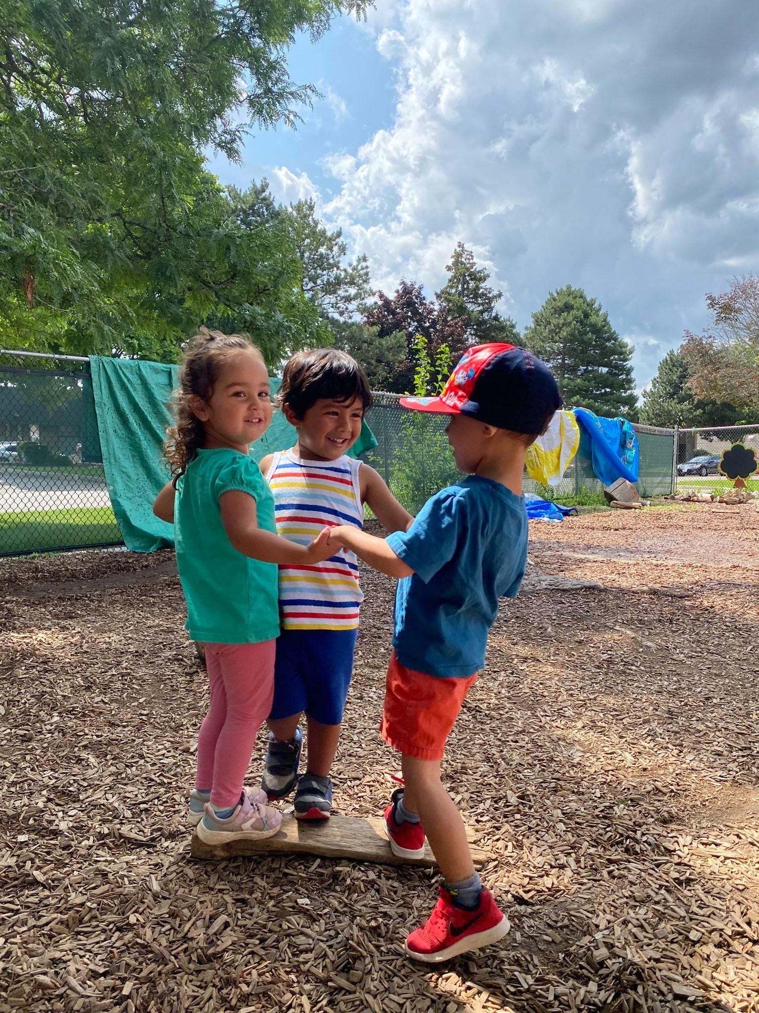Three young children are standing next to each other in a park.
