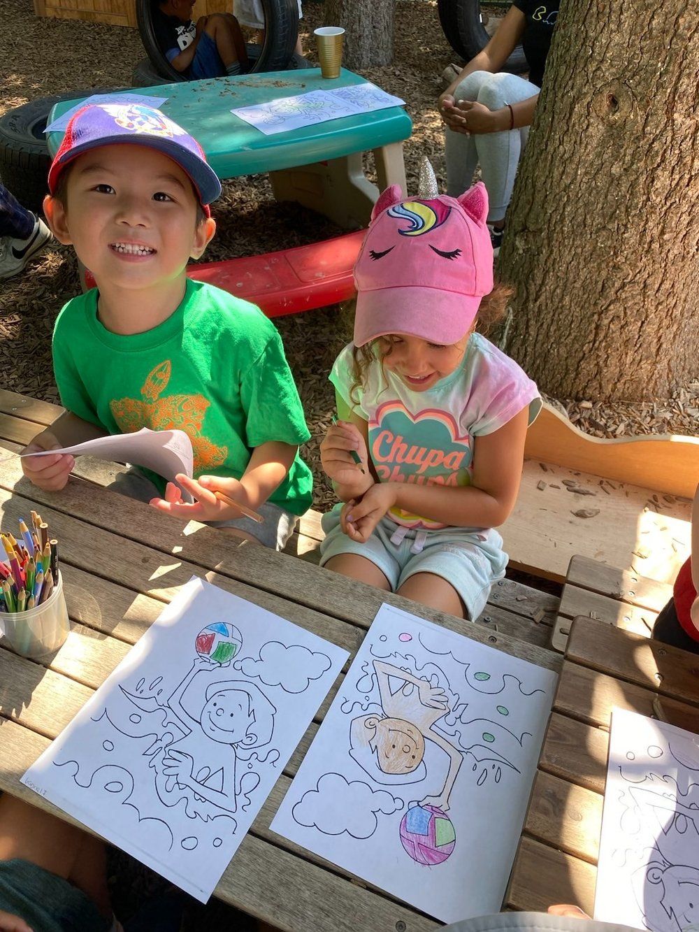 A boy and a girl are sitting at a picnic table drawing.