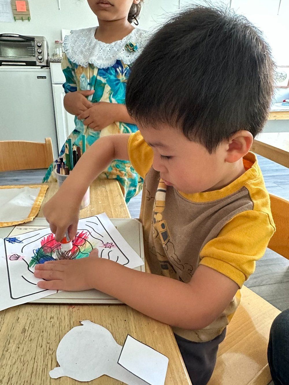 A young boy is sitting at a table playing with a piece of paper.