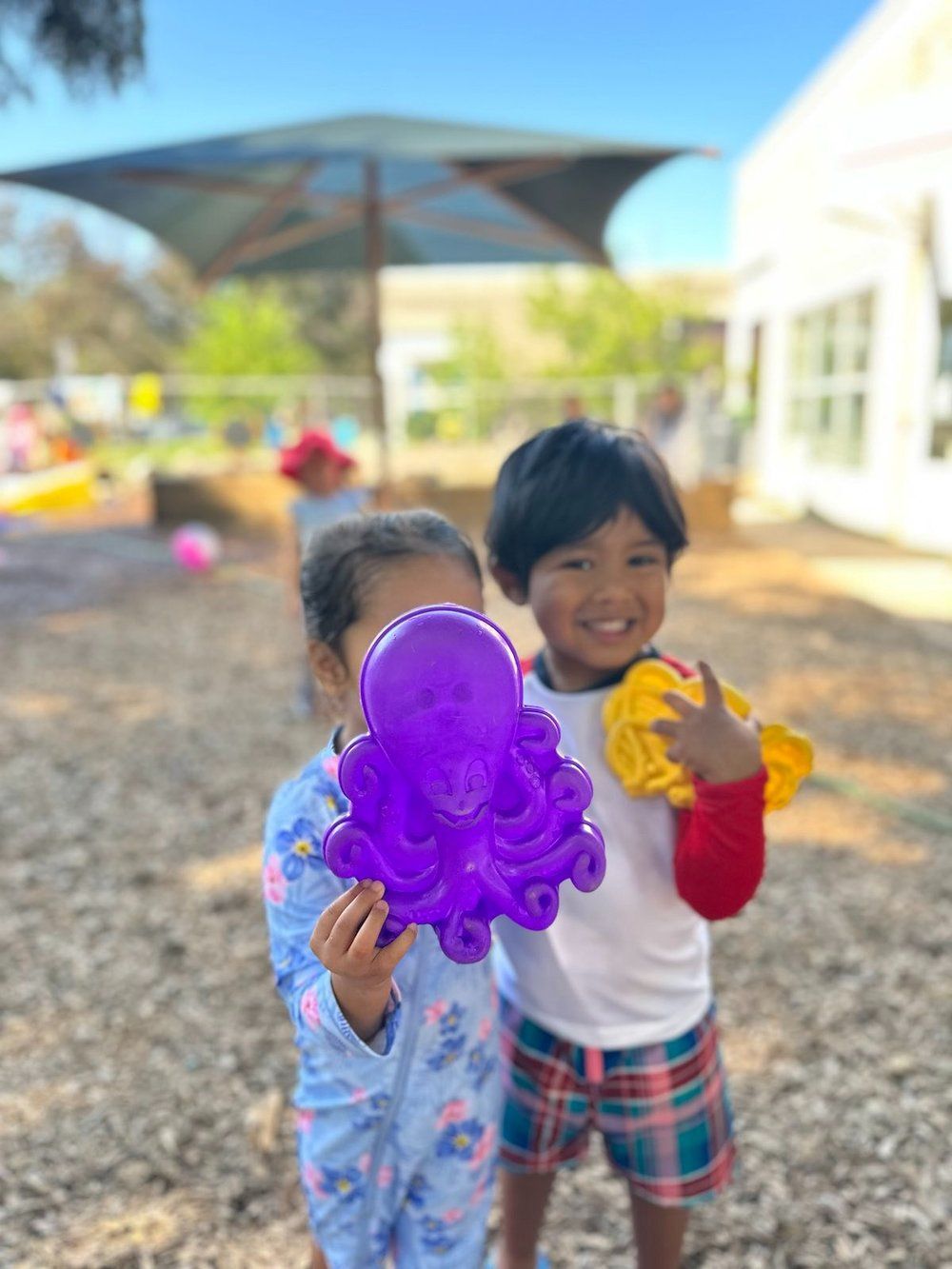A boy and a girl are standing next to each other holding a purple octopus toy.