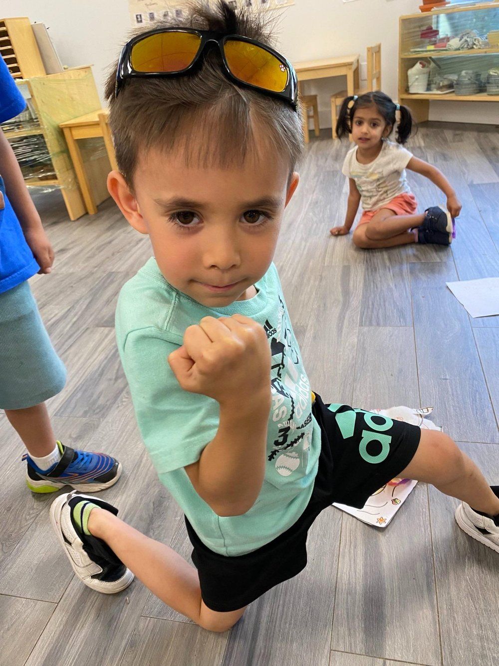 A young boy wearing sunglasses is kneeling on the floor.