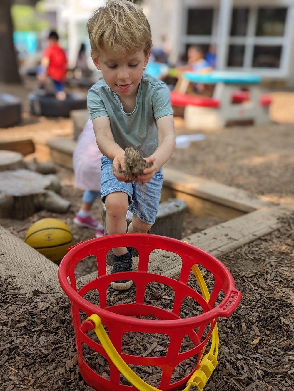 A young boy is playing in the dirt with a red bucket.