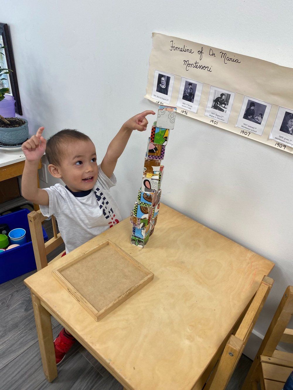 A young boy is sitting at a wooden table playing with blocks.