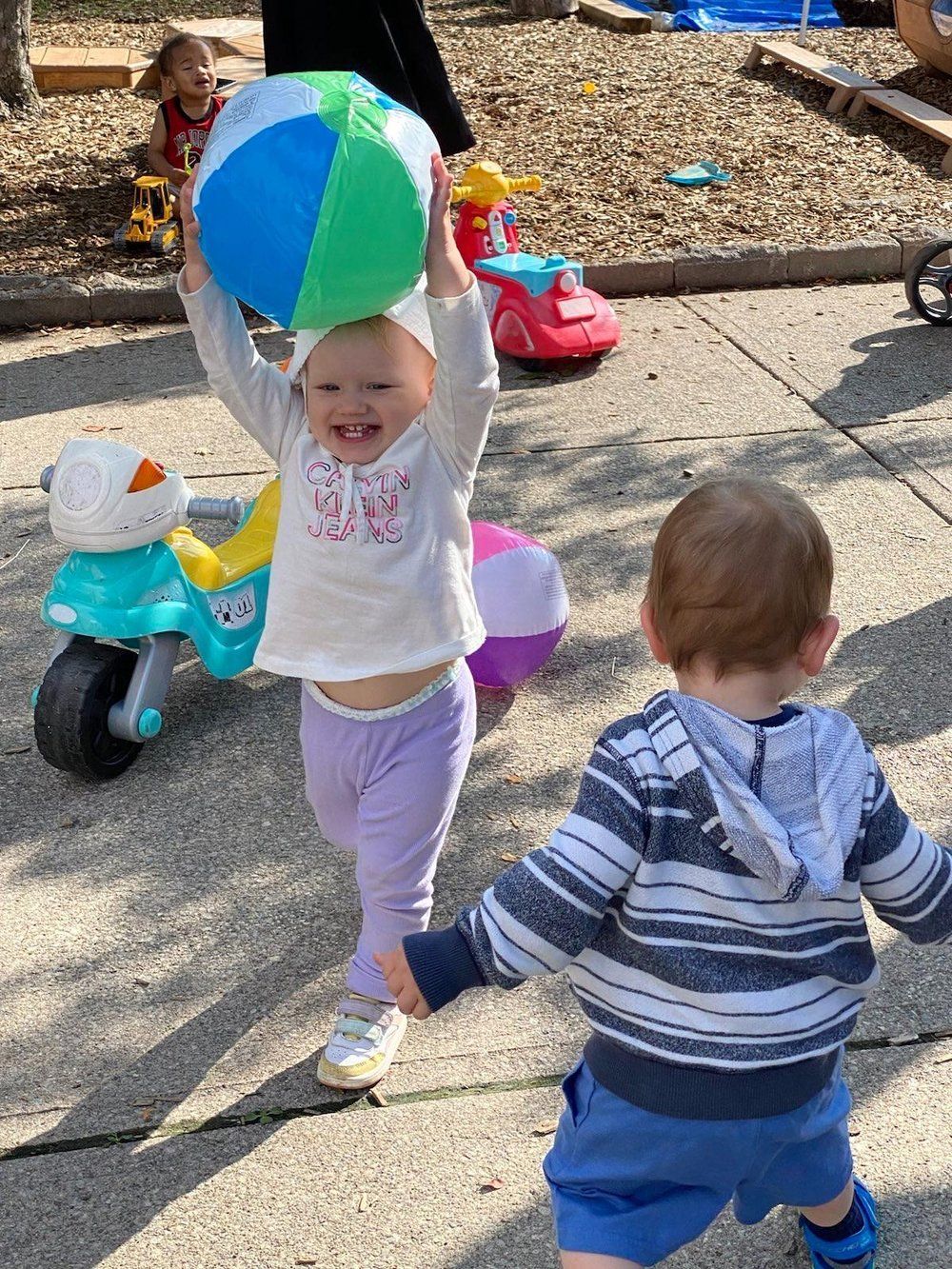 A little girl is holding a beach ball over her head.