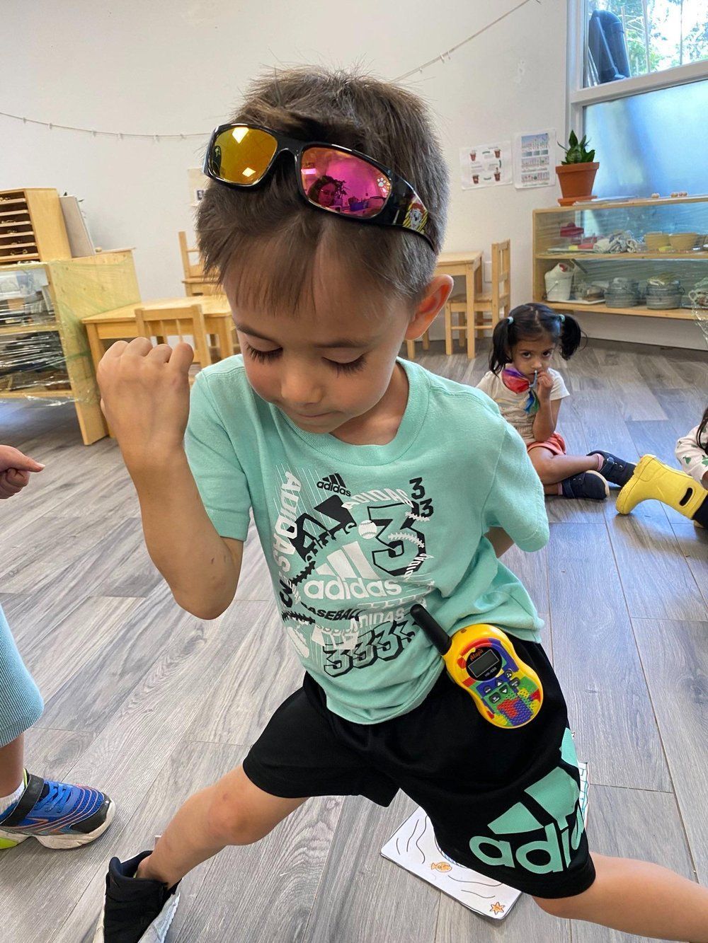 A young boy wearing sunglasses and a walkie talkie is dancing in a room.