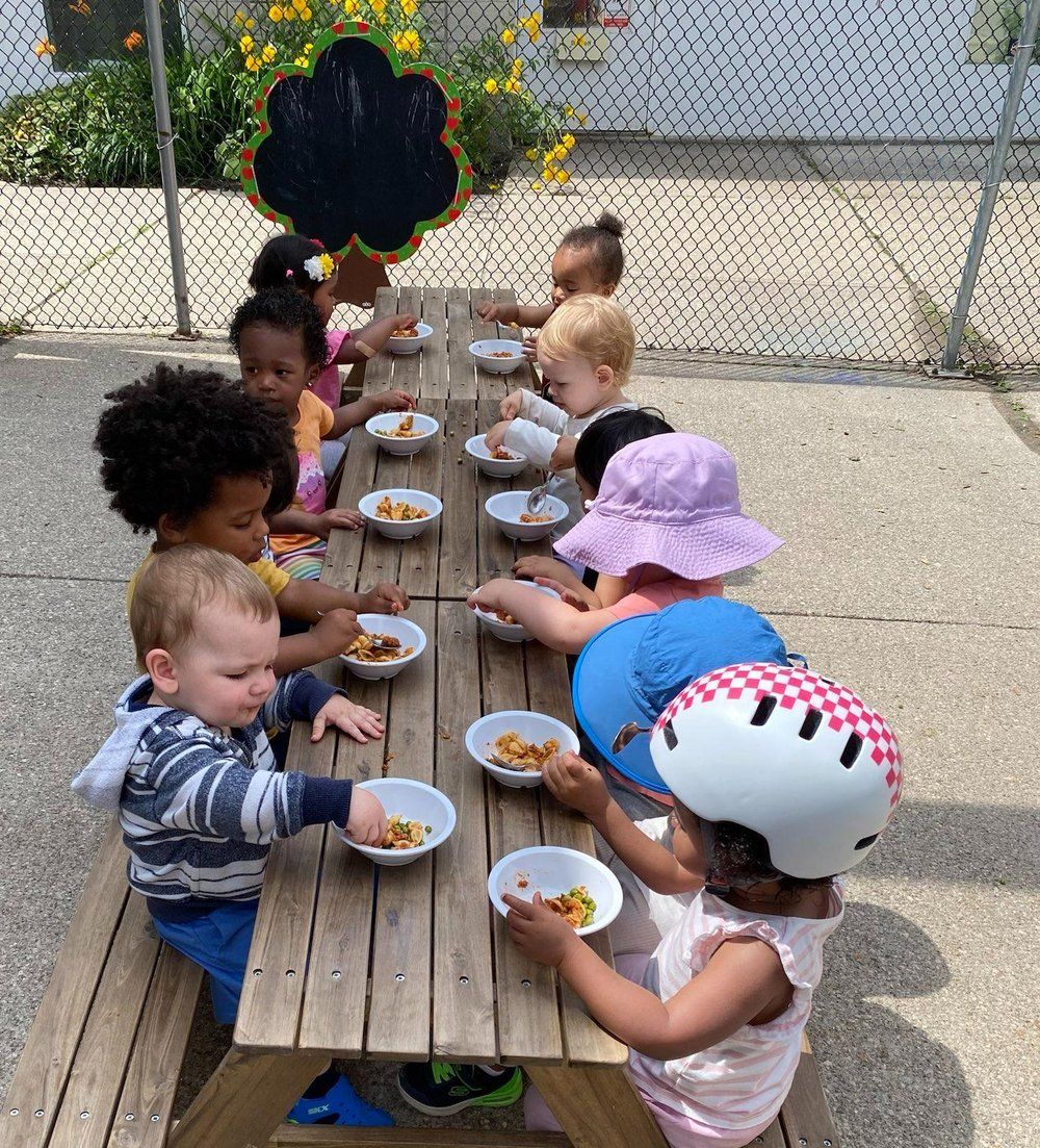 A group of children are sitting at a picnic table eating food.