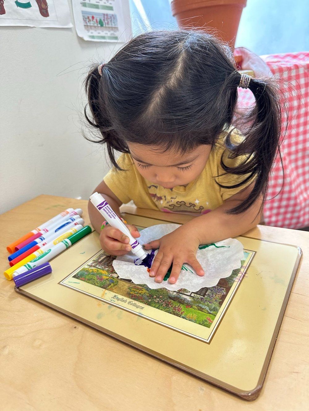A little girl is sitting at a table drawing with markers.