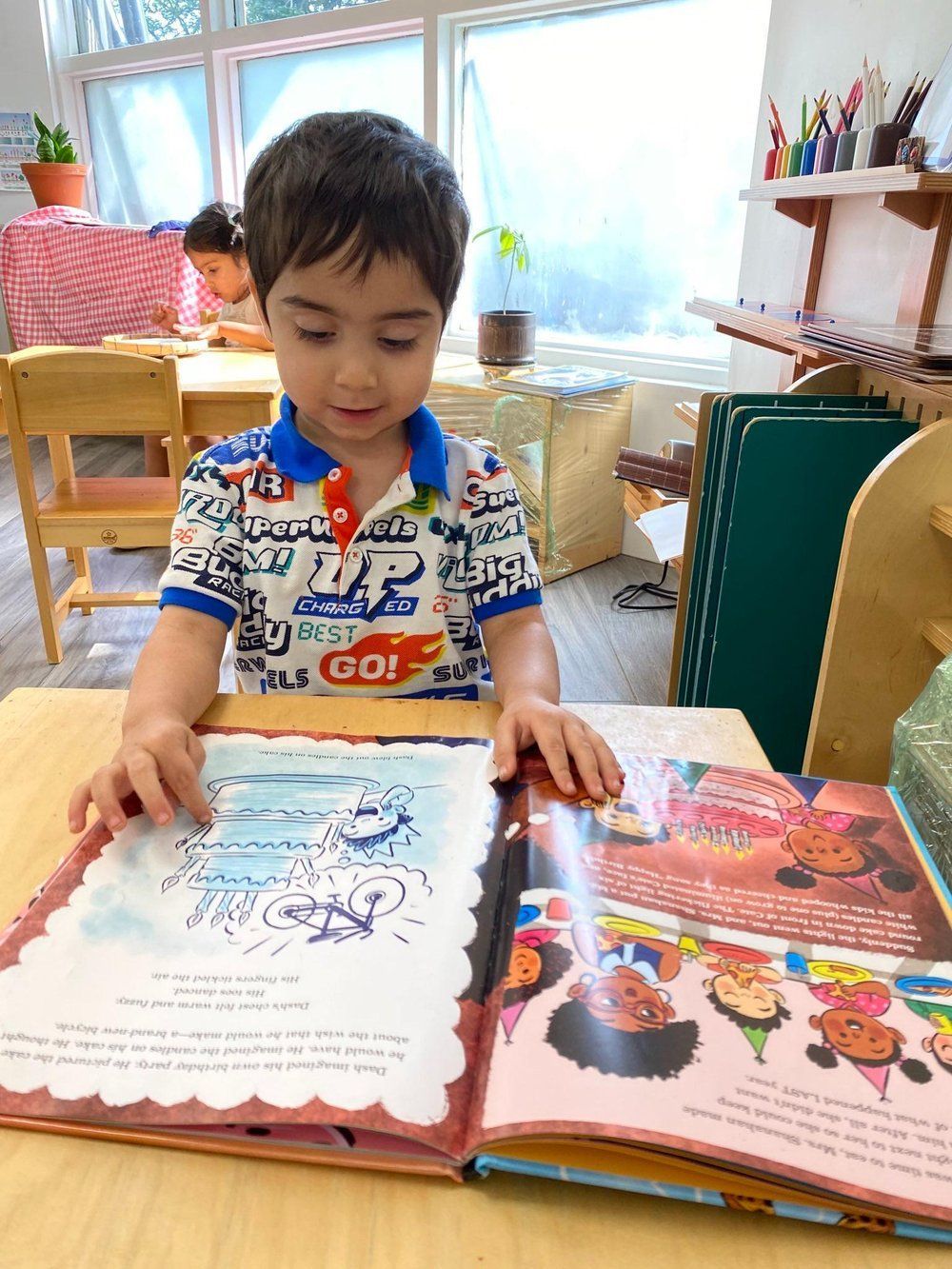 A young boy is sitting at a table reading a book.