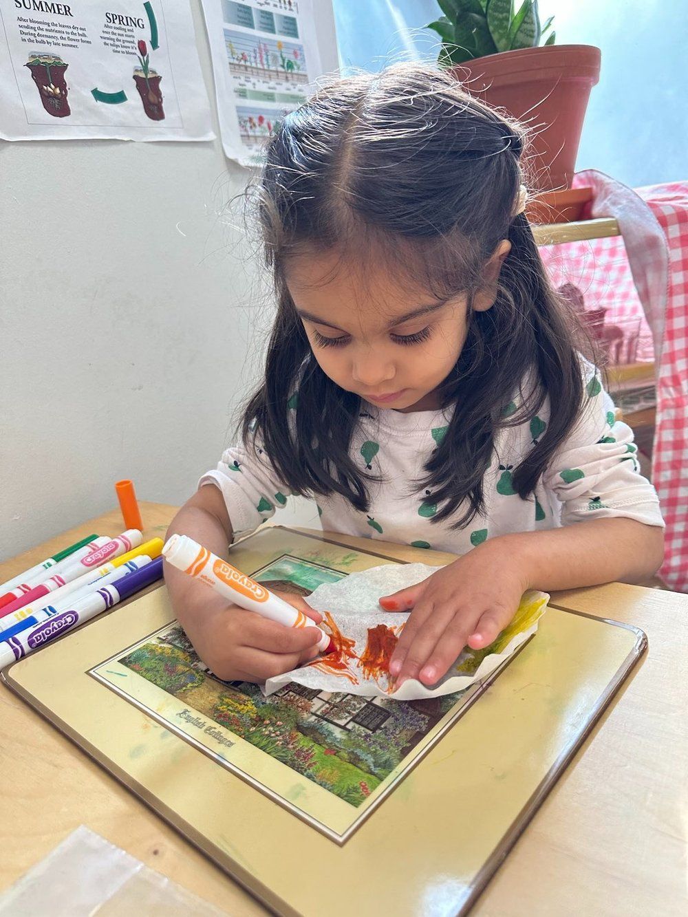 A little girl is sitting at a table drawing with markers.