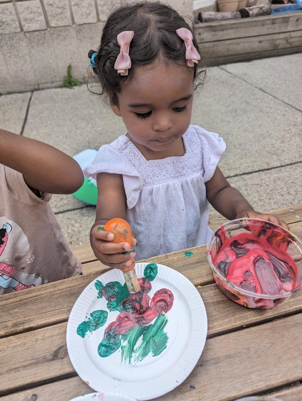 A little girl is painting on a paper plate with a brush.
