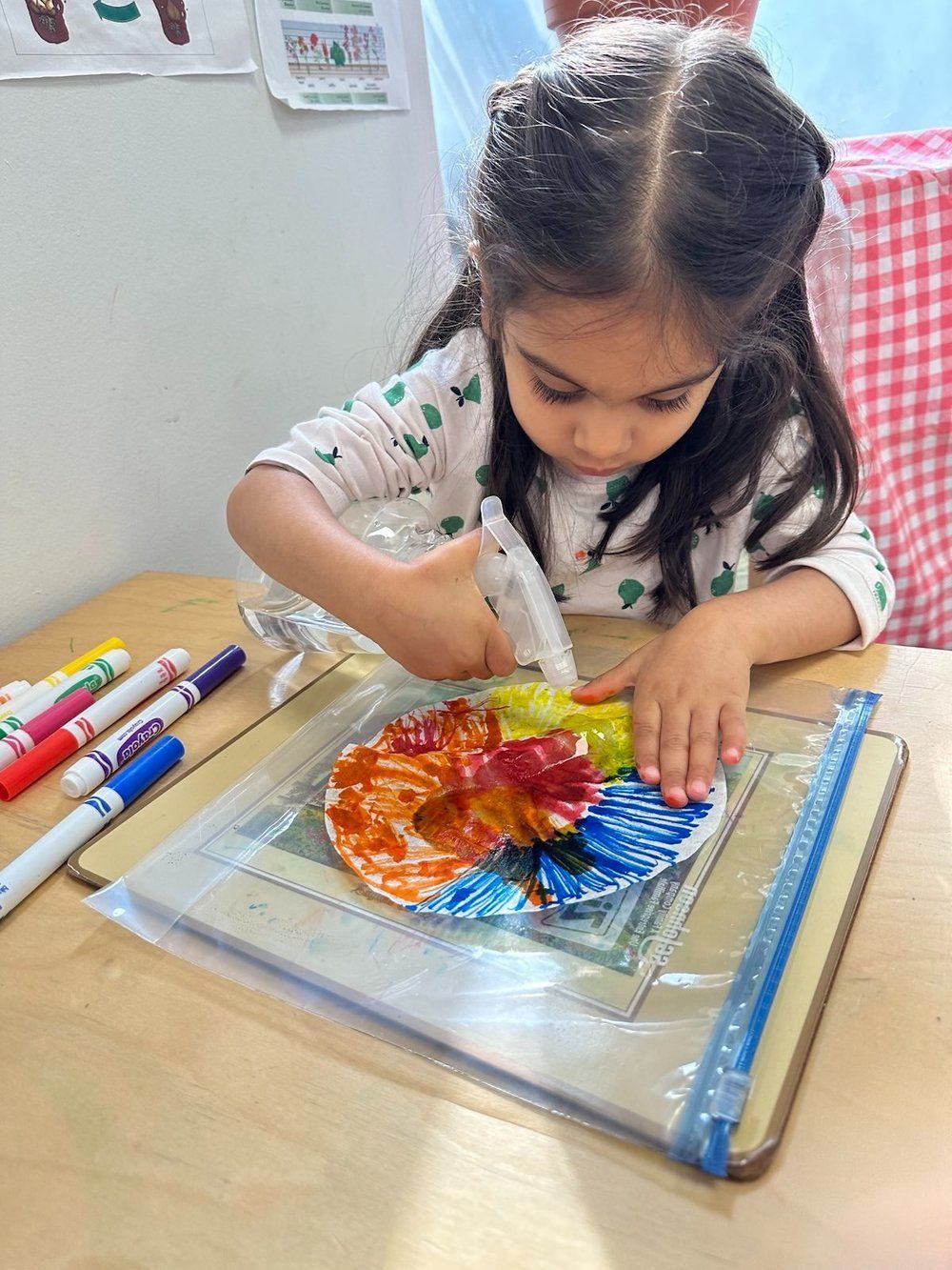 A little girl is sitting at a table painting with markers.