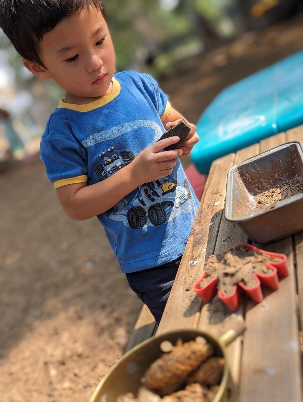 A young boy in a blue shirt is playing with sand on a picnic table.