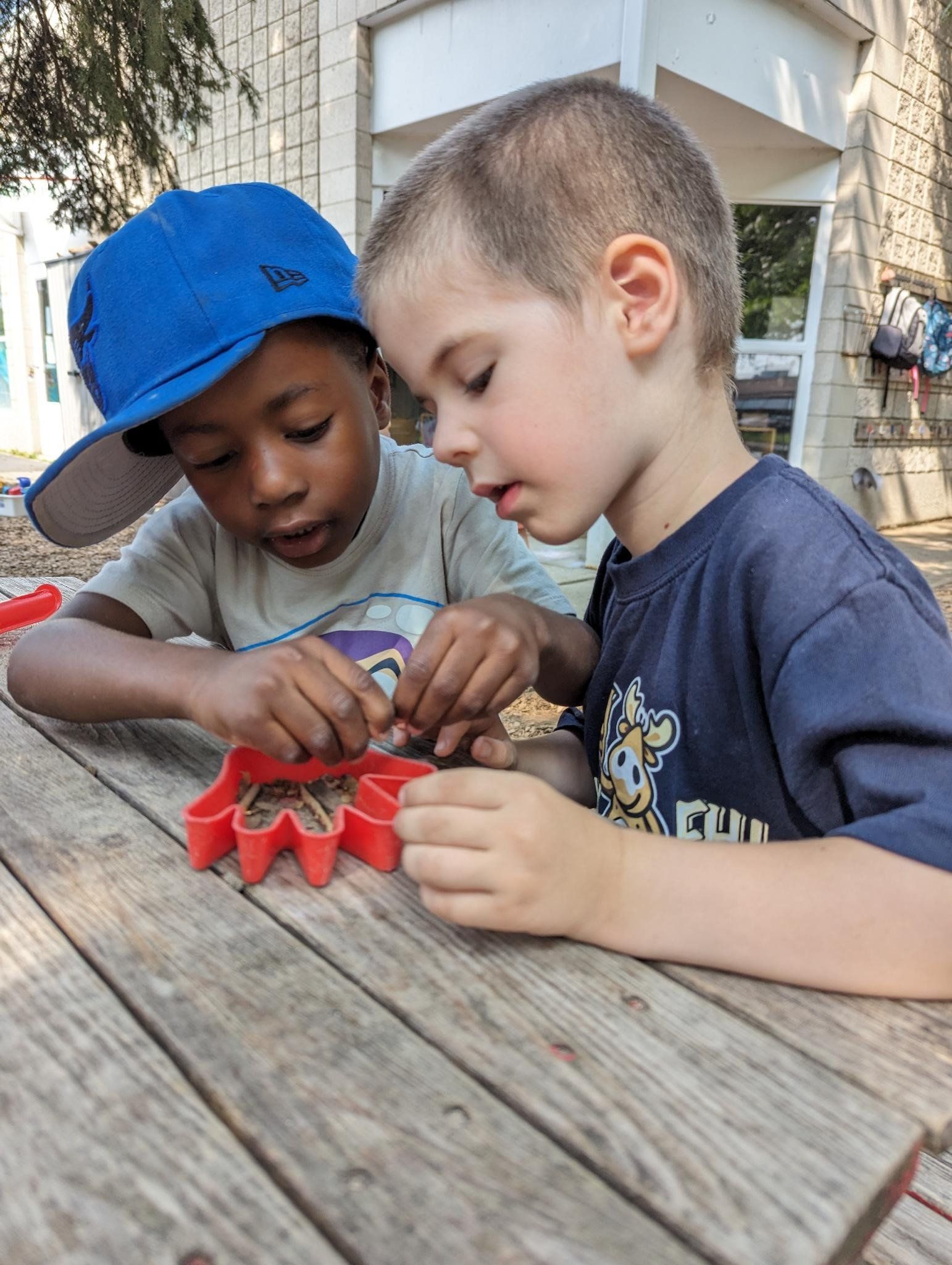 Two young boys are sitting at a wooden table playing with cookie cutters.