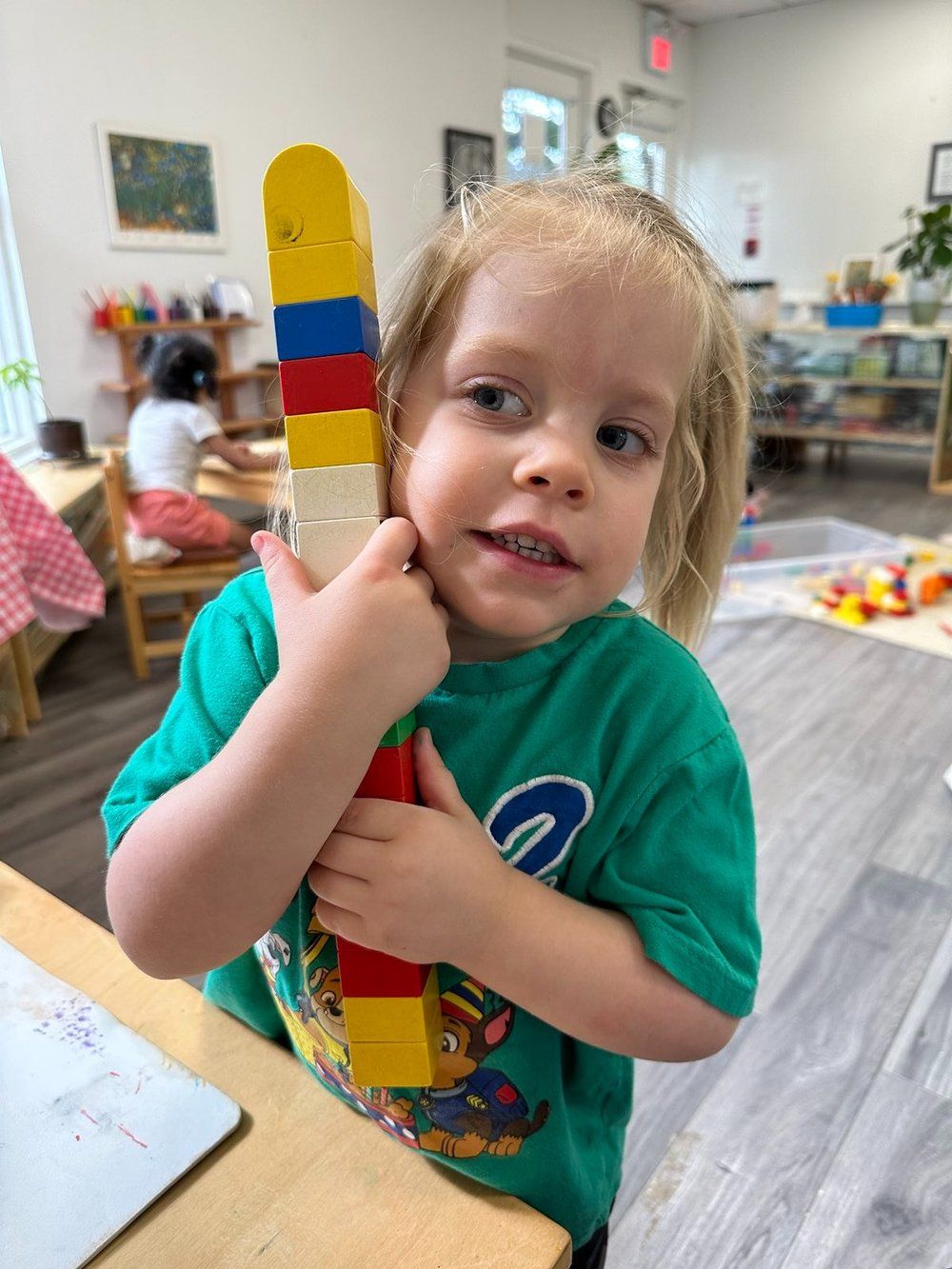 A little girl in a green shirt is holding a stack of lego blocks.