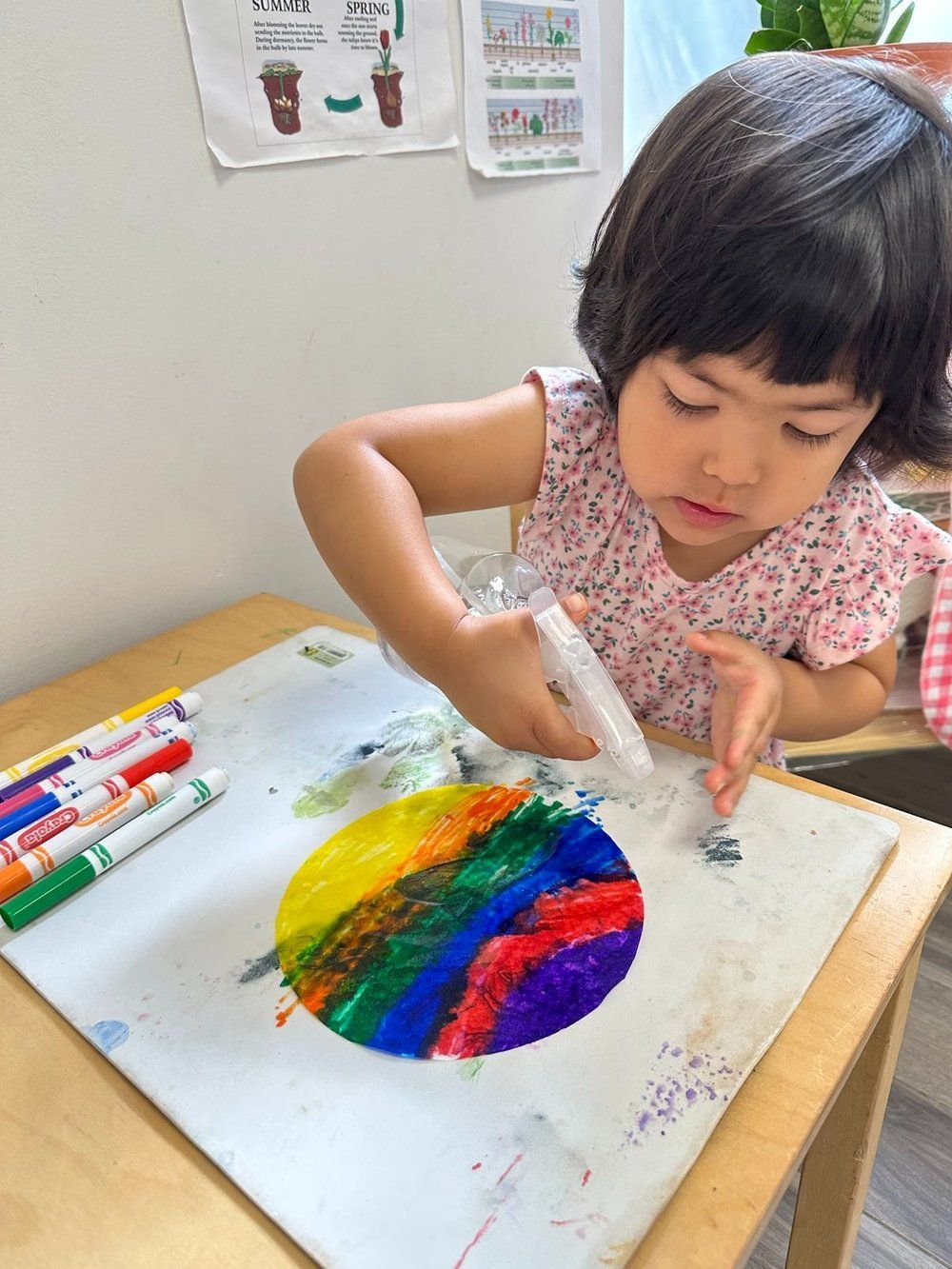 A little girl is sitting at a table painting with markers.