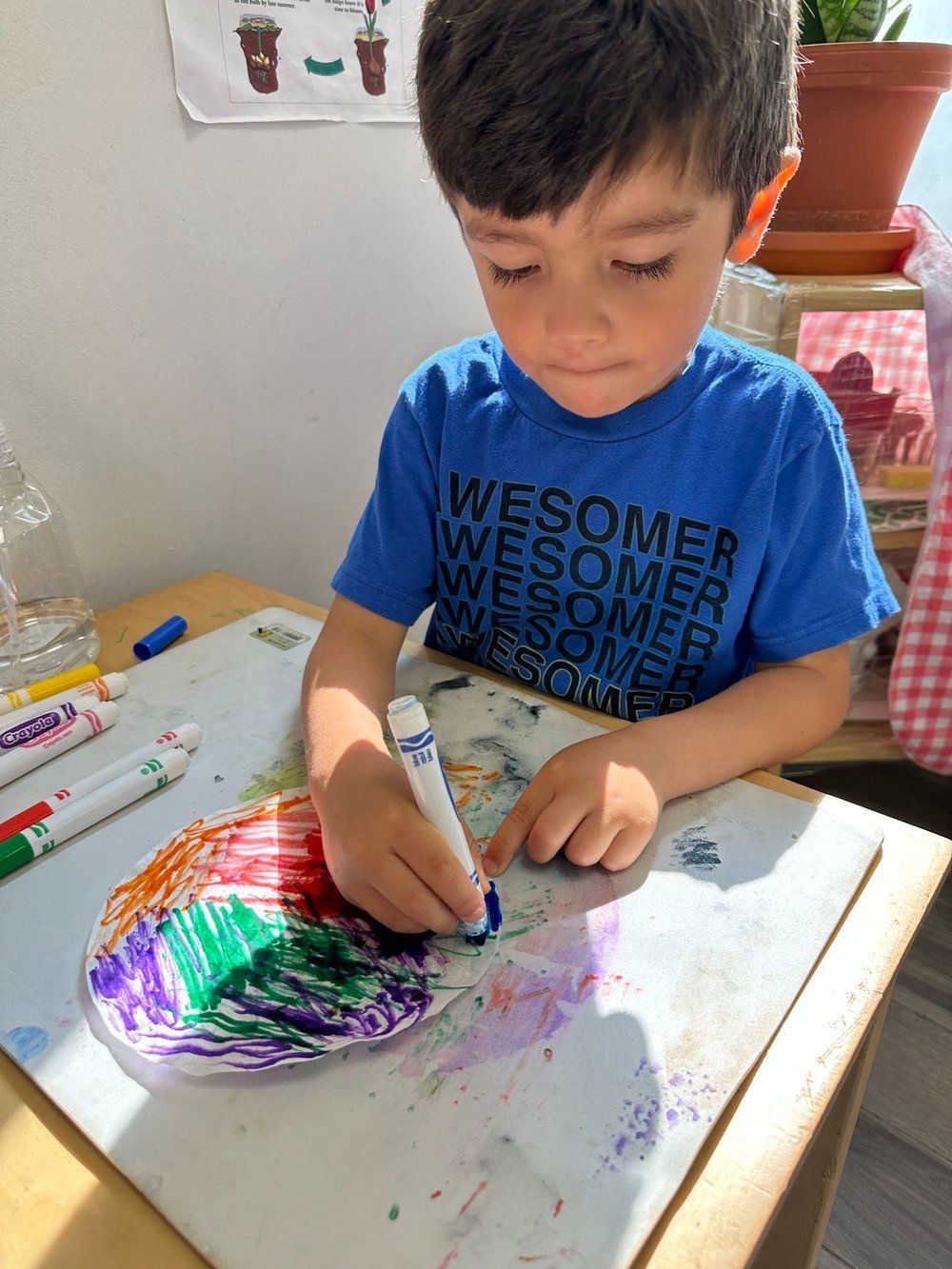 A young boy is sitting at a table drawing with markers.
