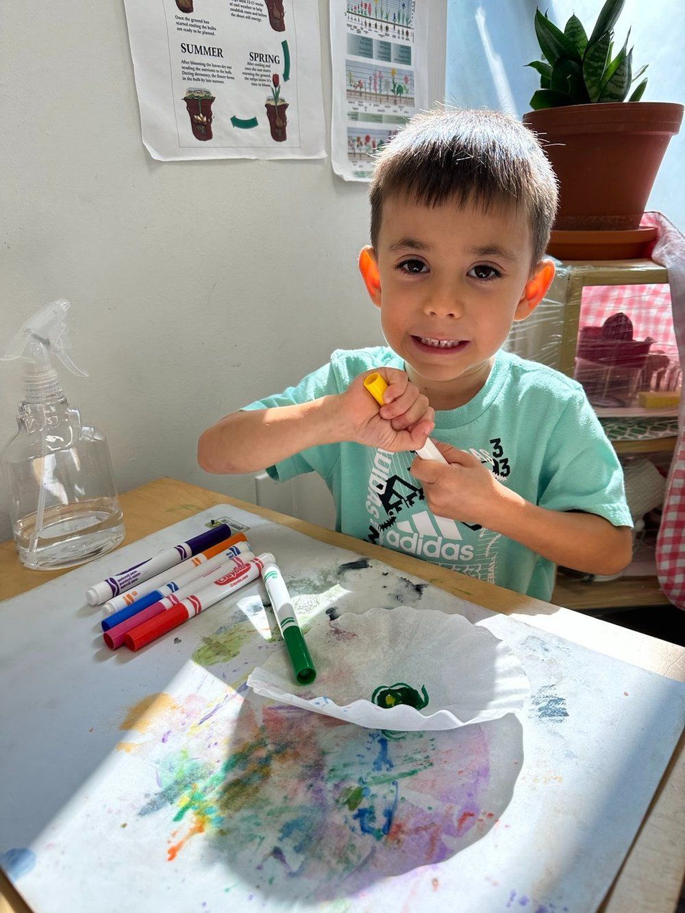 A young boy is sitting at a table with markers and paper plates.