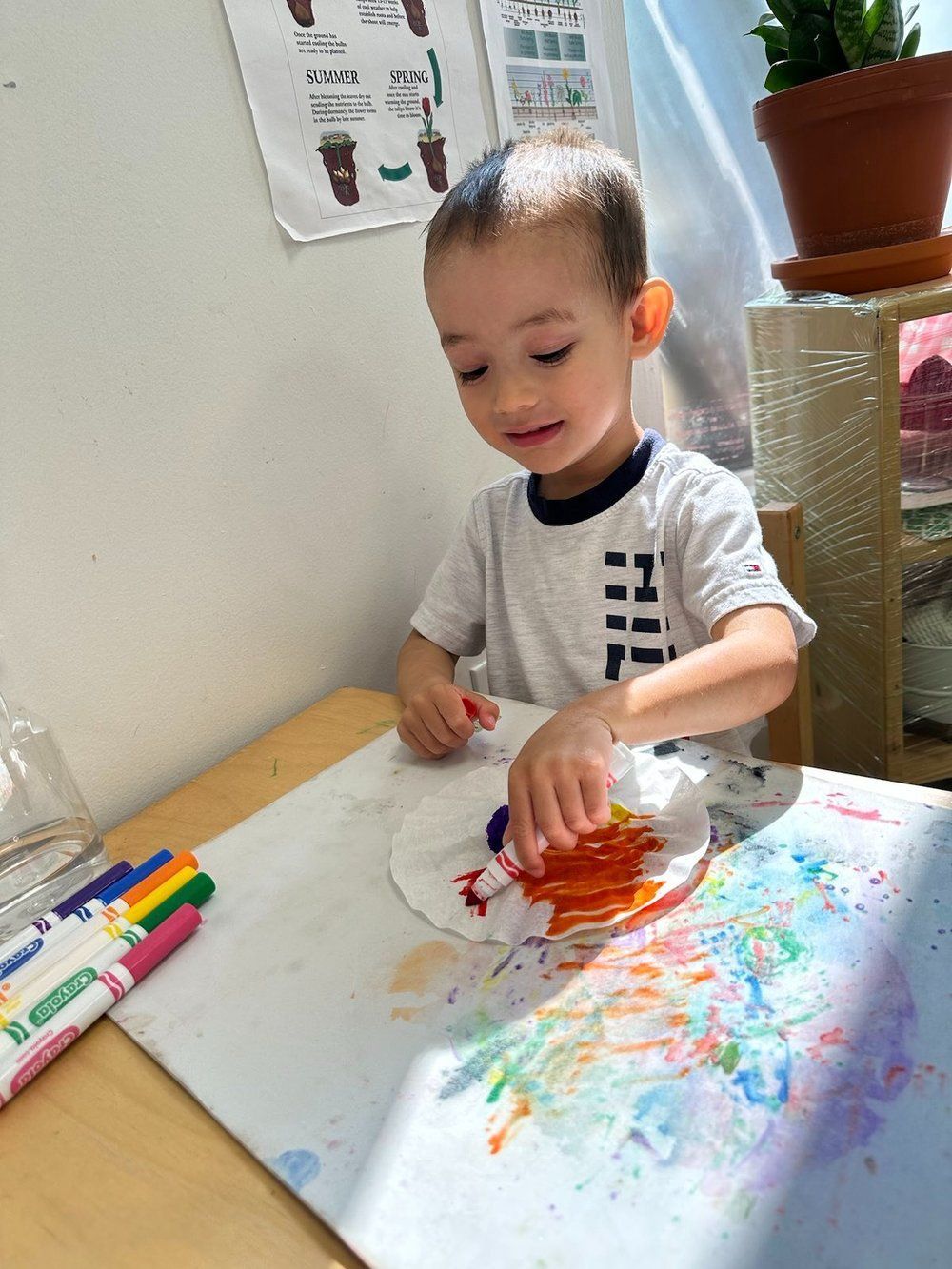 A young boy is sitting at a table painting on a paper plate.