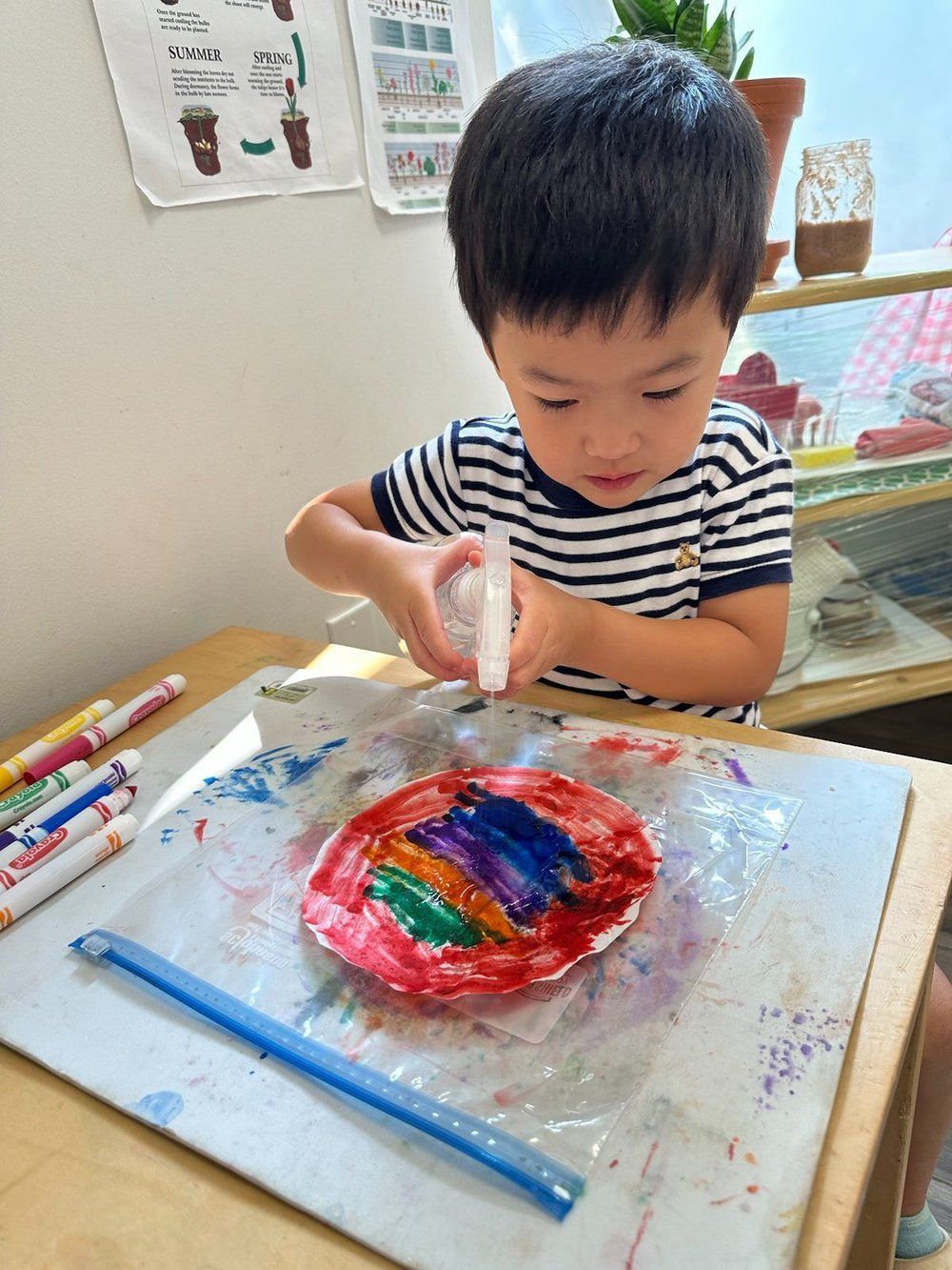 A young boy is sitting at a table painting with a brush.