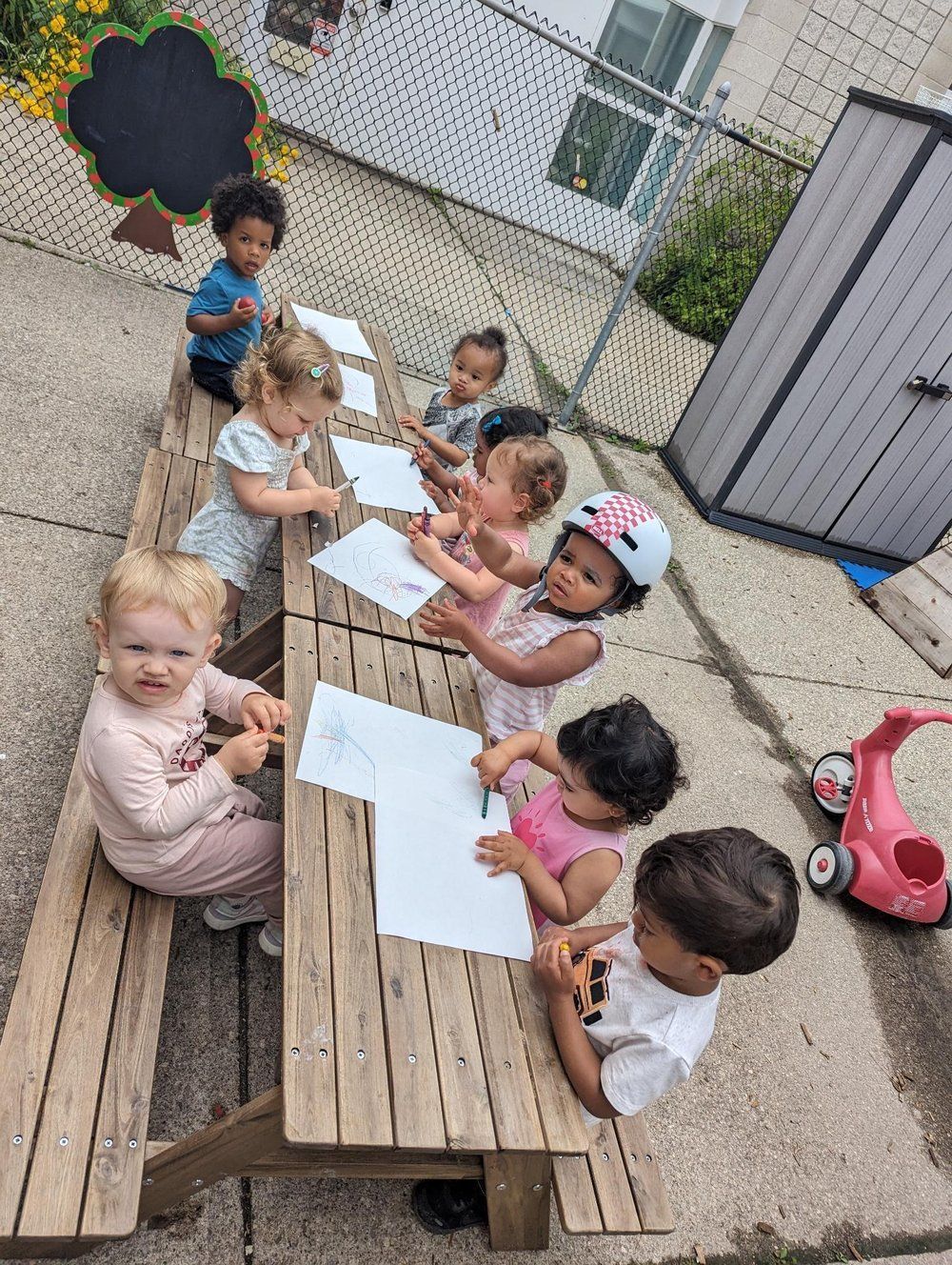 A group of children are sitting at a wooden picnic table.
