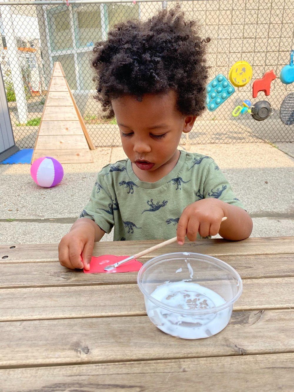 A young boy is playing with glue on a wooden table.