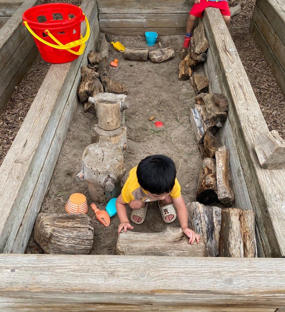 A young boy is playing in a wooden sandbox.