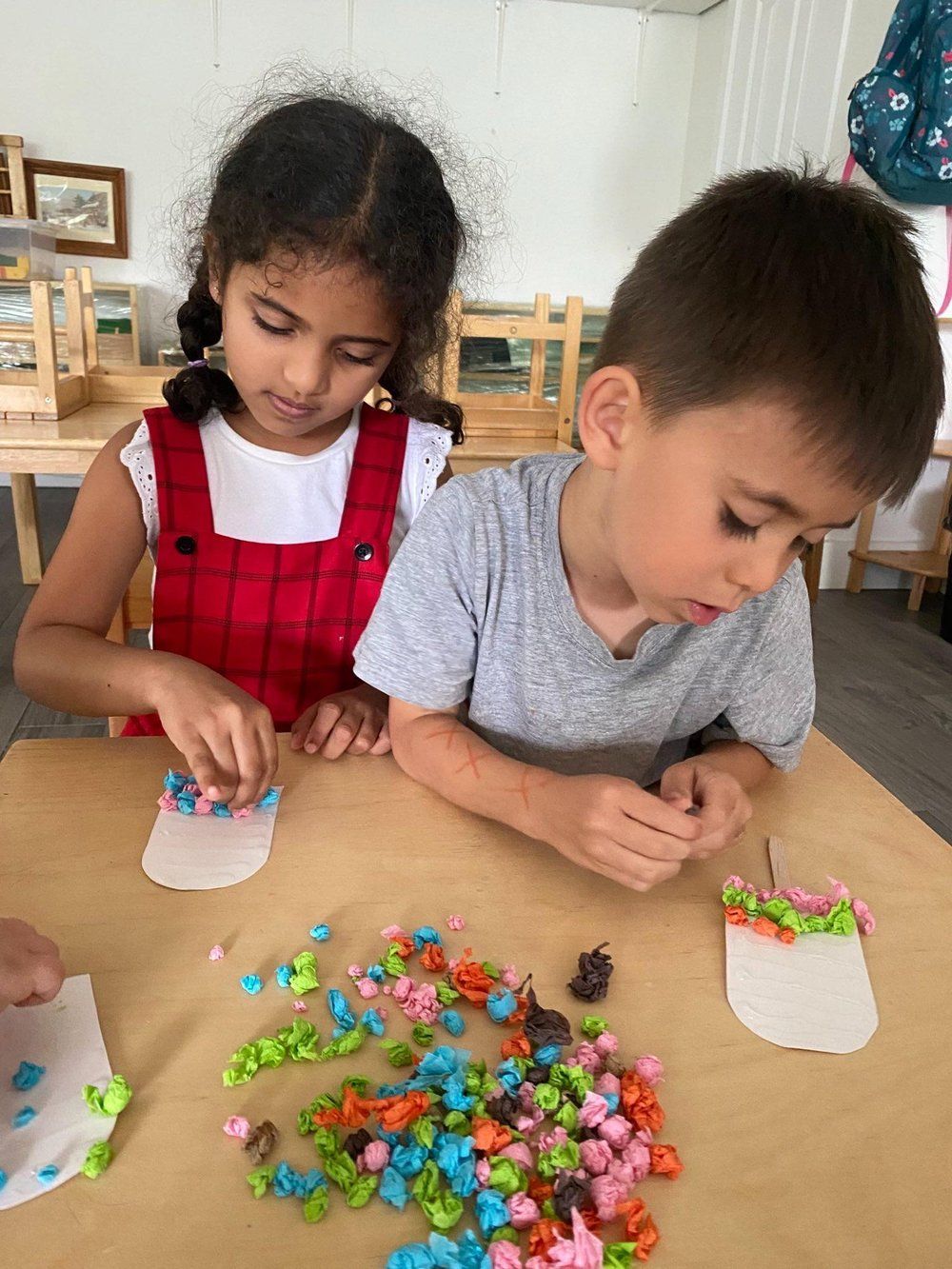A boy and a girl are sitting at a table playing with beads.