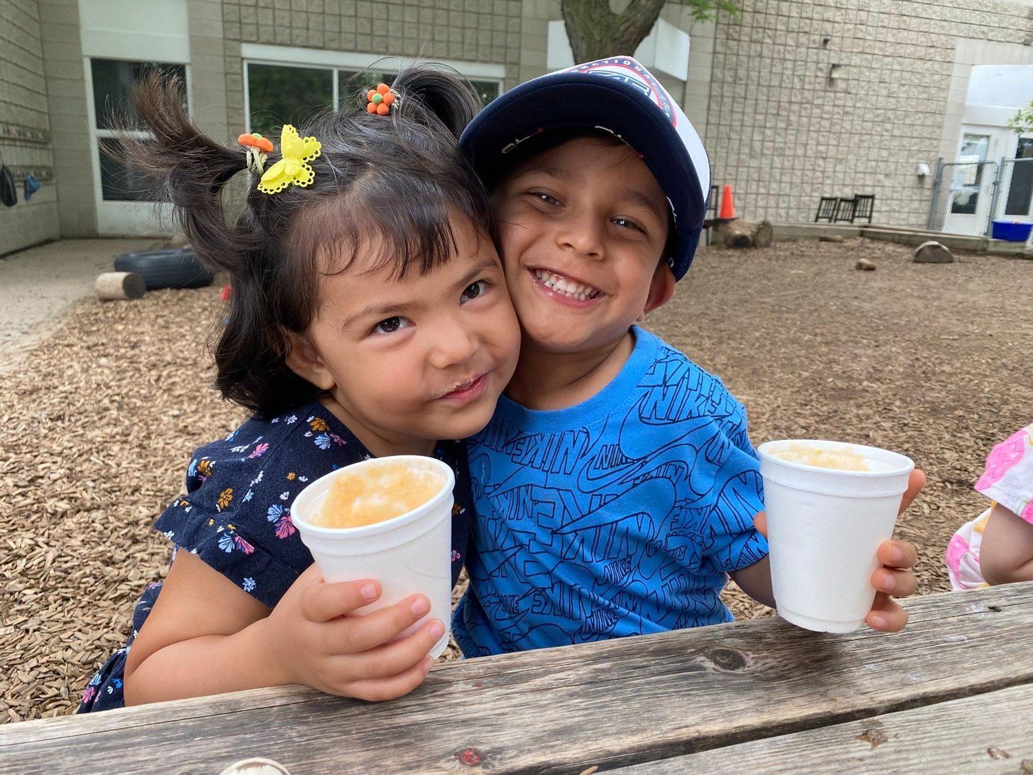 A boy and a girl are sitting at a picnic table holding cups of coffee.