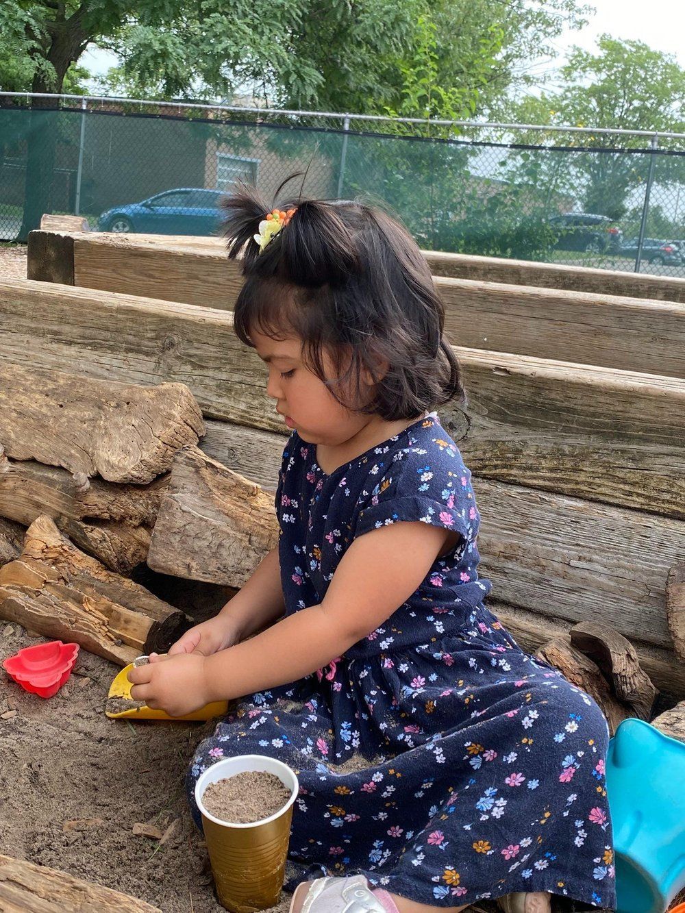 A little girl is sitting on the ground playing in the sand.