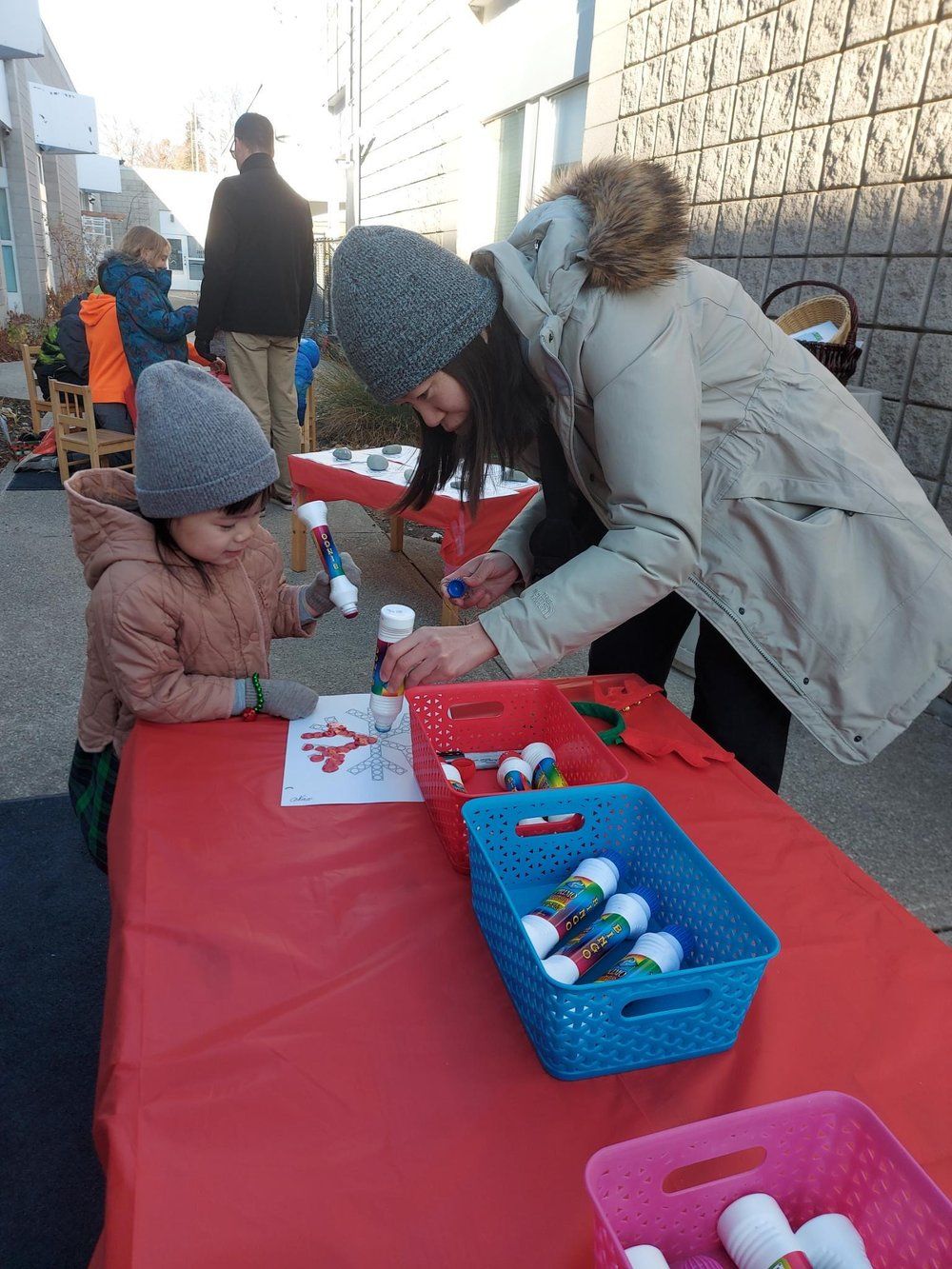A woman is helping a child with a craft at a table.