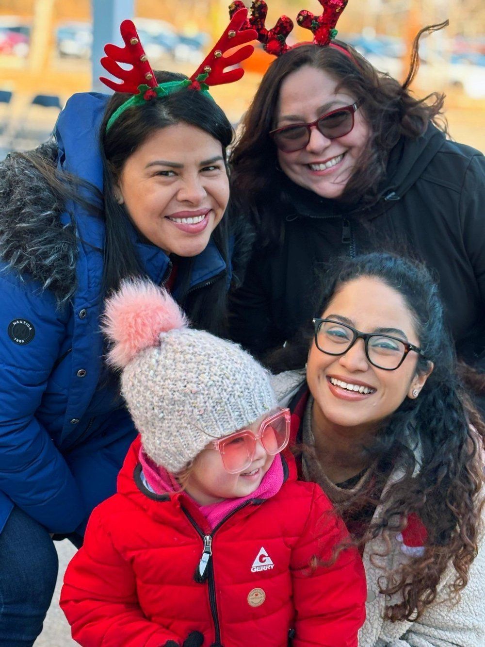 A group of women are posing for a picture with a little girl wearing a reindeer headband.