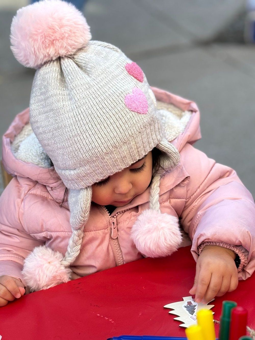 A little girl wearing a hat and a pink jacket is sitting at a table