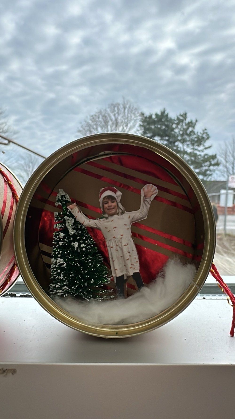 A christmas ornament with a picture of a little girl standing next to a christmas tree.