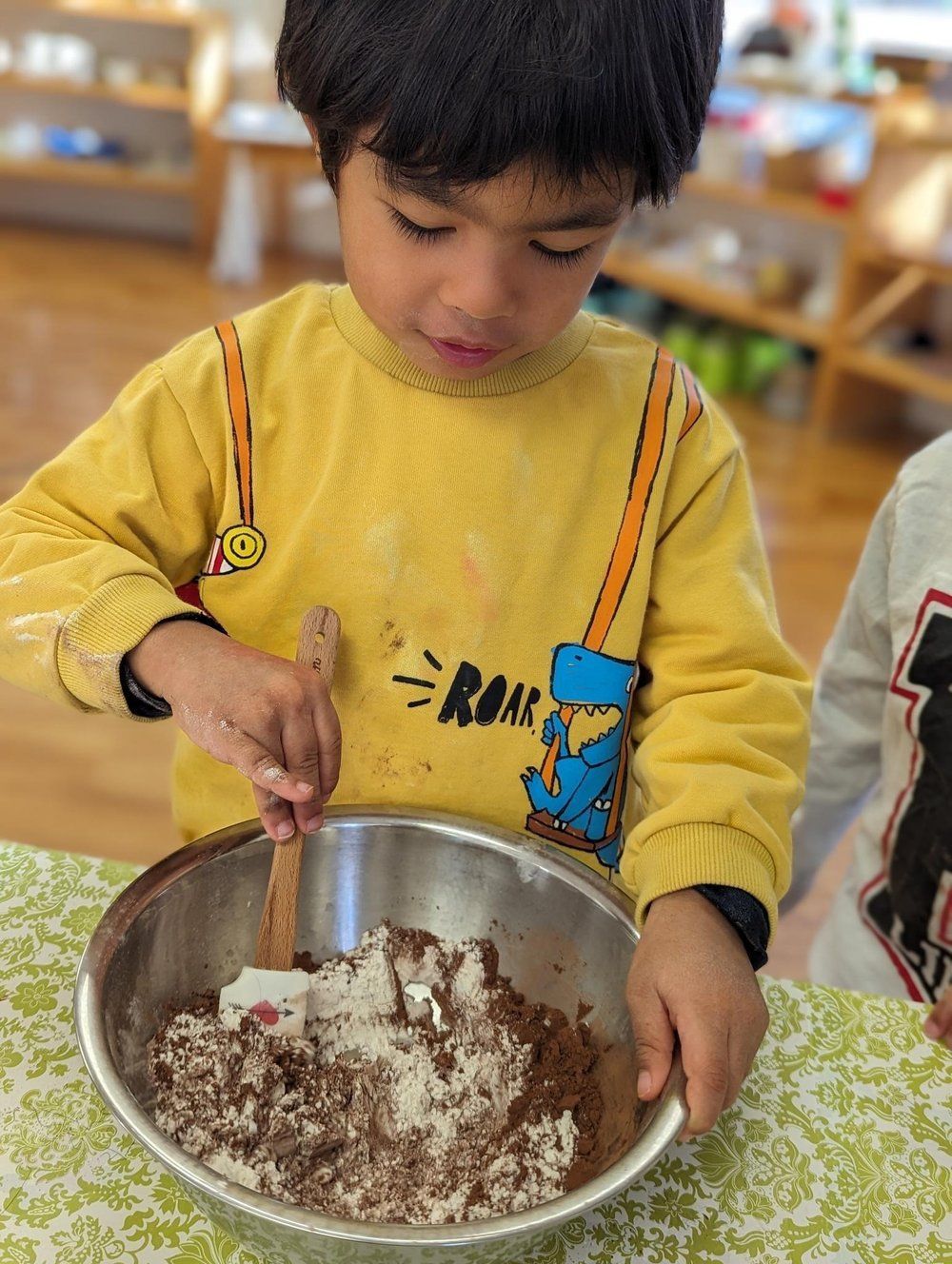A young boy is mixing ingredients in a bowl with a spatula.