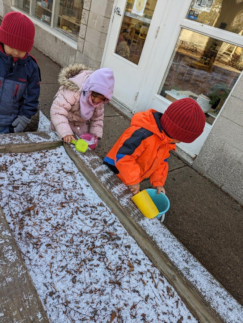 A group of children are playing in the snow with buckets and shovels.