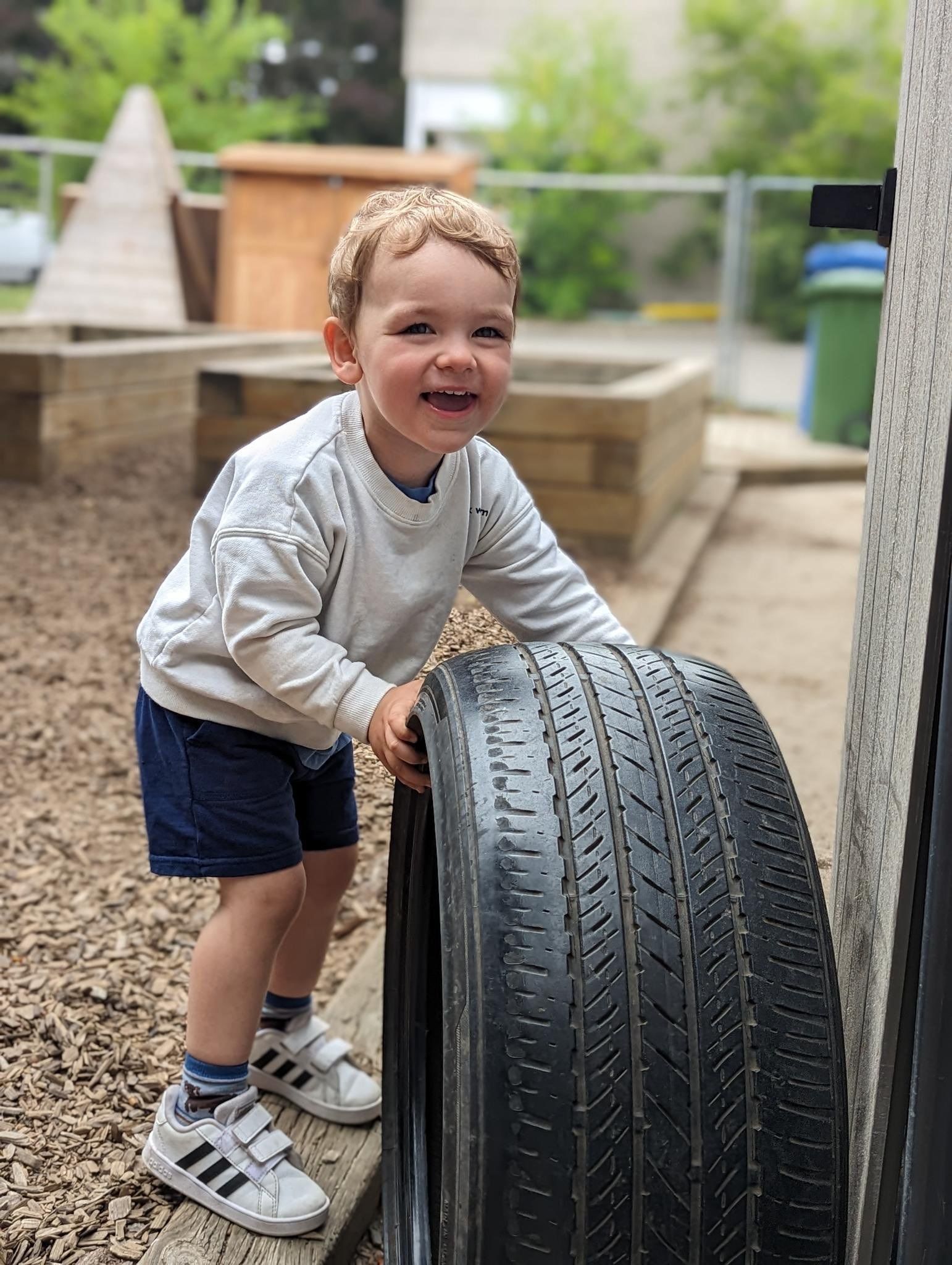 A young boy is playing with a tire in a playground.