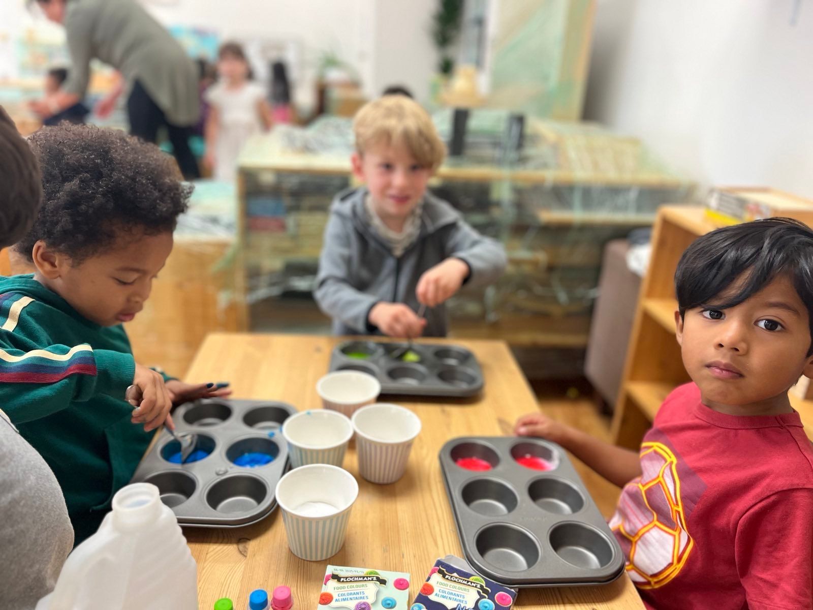 A group of children are sitting at a table making cupcakes.