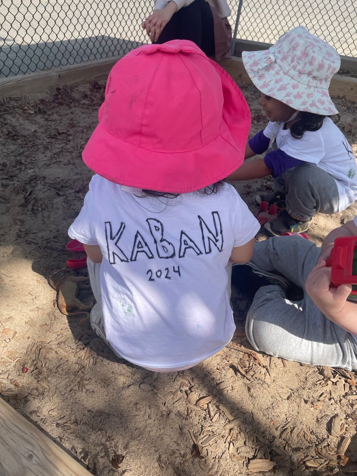 A little girl wearing a pink hat is playing in a sandbox.