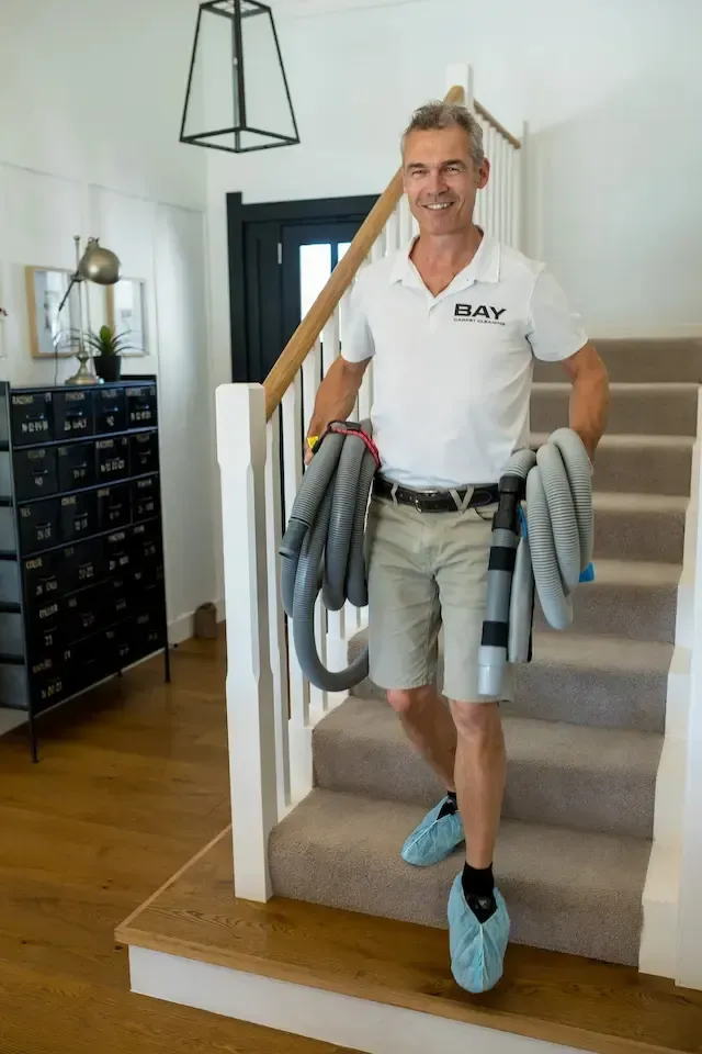 Man standing on a staircase holding coiled hoses, wearing a white shirt, shorts, and blue shoe covers.