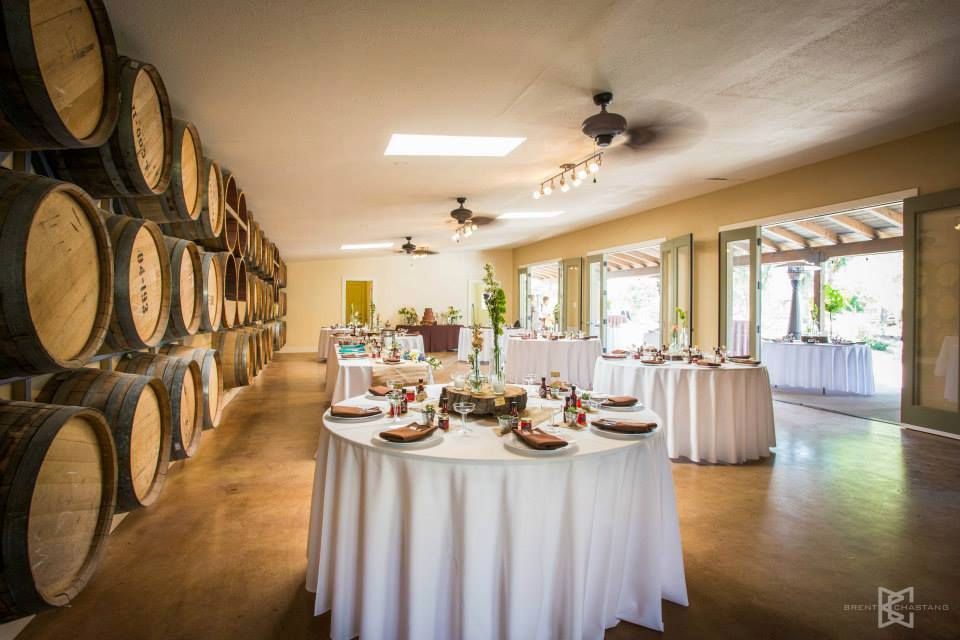 Wine barrels line one wall of a room with round tables set for a gathering, open doors to patio.