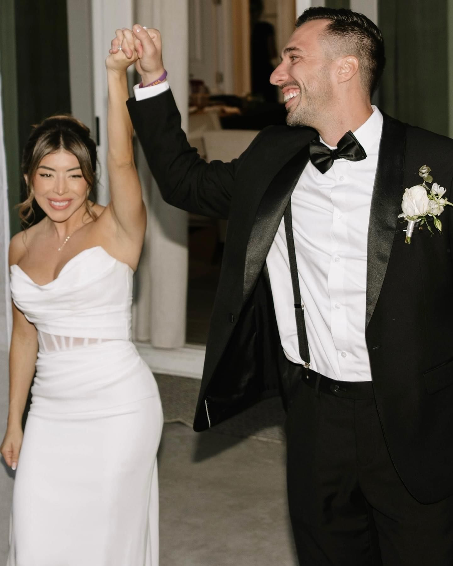 Couple at outdoor wedding ceremony, under arch with white fabric, chairs decorated.