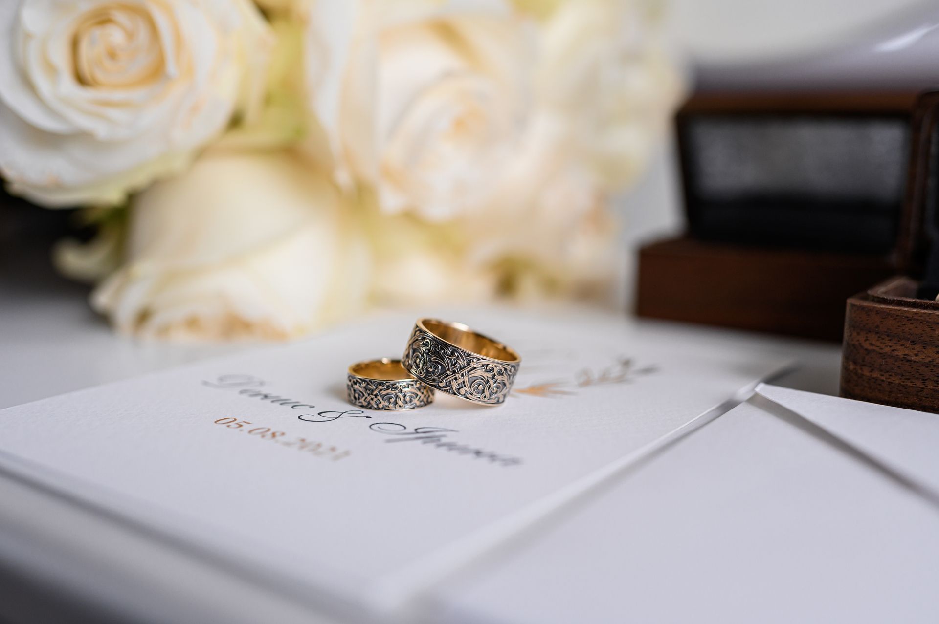 Two wedding rings on a white card beside white roses