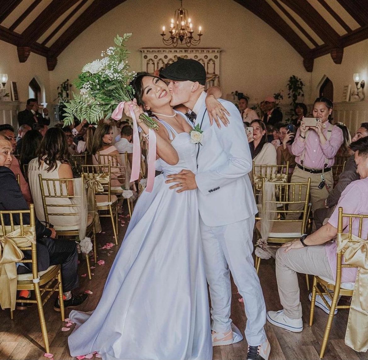 Wedding table with white chairs, draped in white linen and burlap runner, floral centerpiece.
