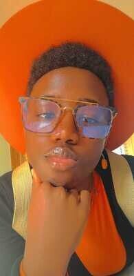 Person with an orange hat and glasses, resting chin on hand, with a pursed lip.
