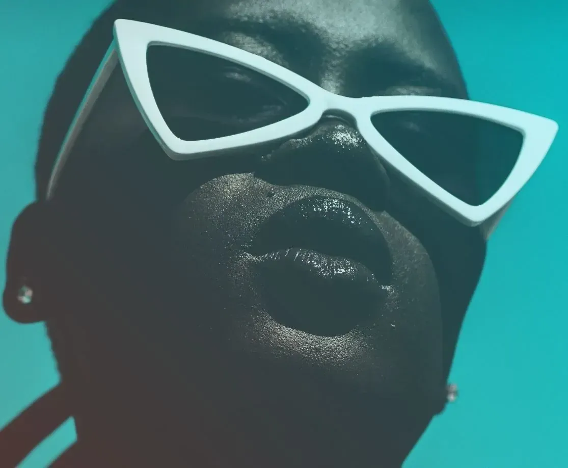 Person with dark skin wearing white sunglasses; glossy lips; blue-green gradient background.