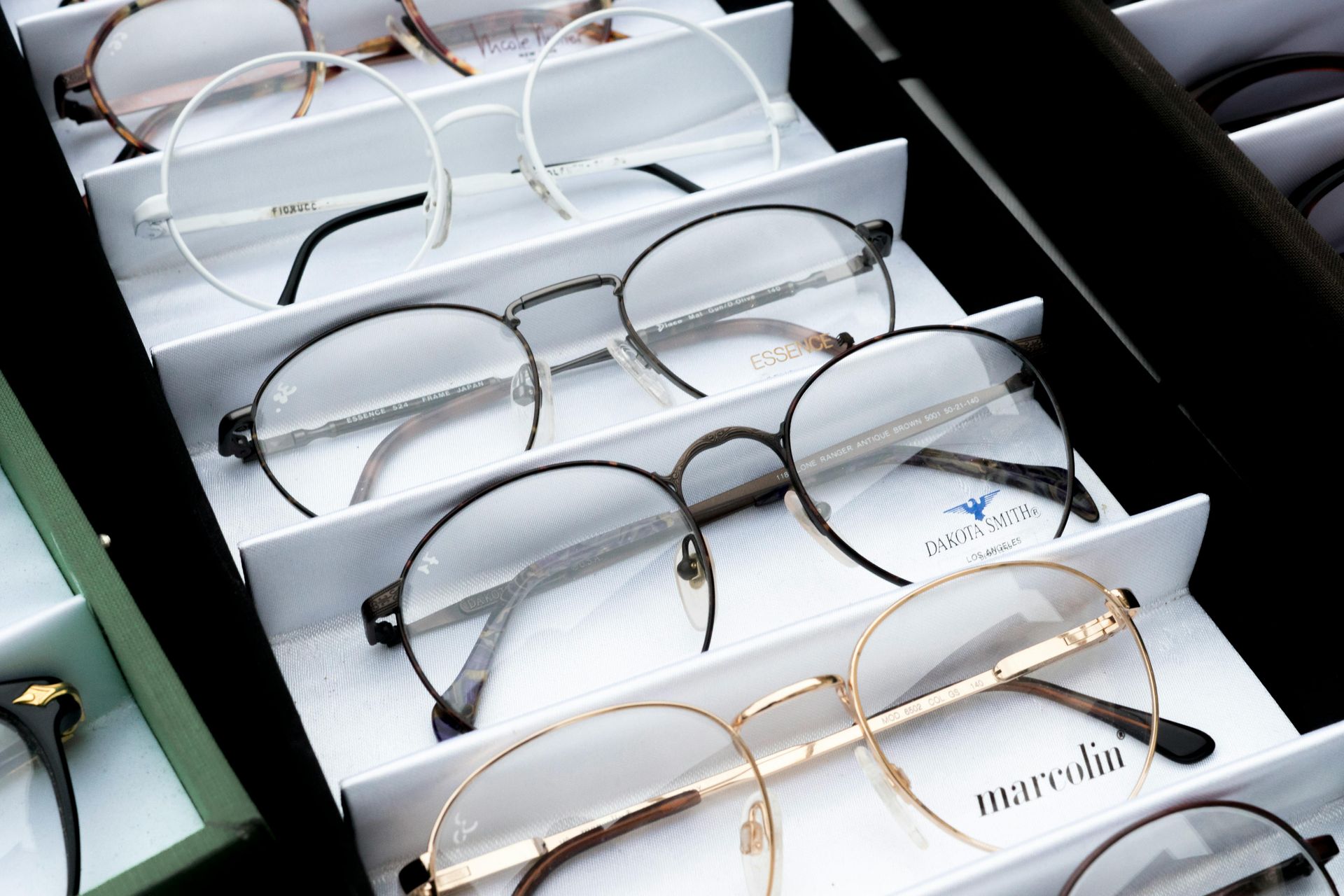 Eyeglasses displayed in a case; various styles and frame colors, including gold and black.