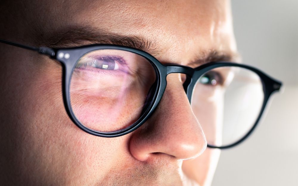 Close-up of a person wearing black-framed glasses, looking intently to the right.