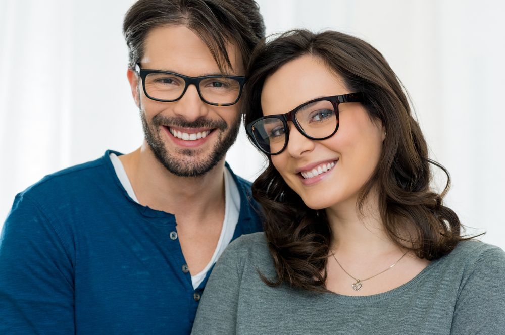 Smiling couple wearing glasses, man in blue, woman in gray, close up.